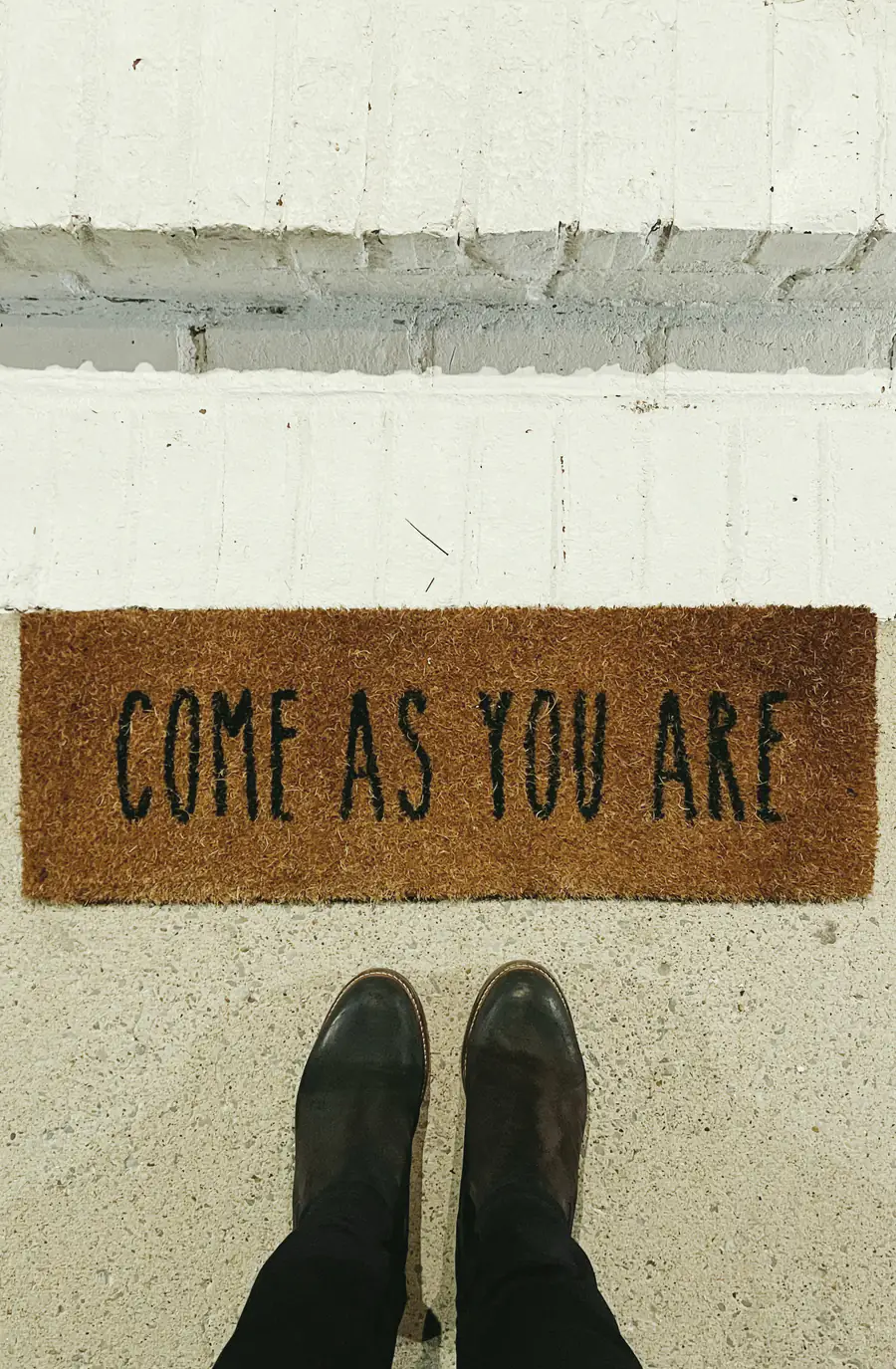 A doormat reading “come as you are” at the top of a set of steps.
