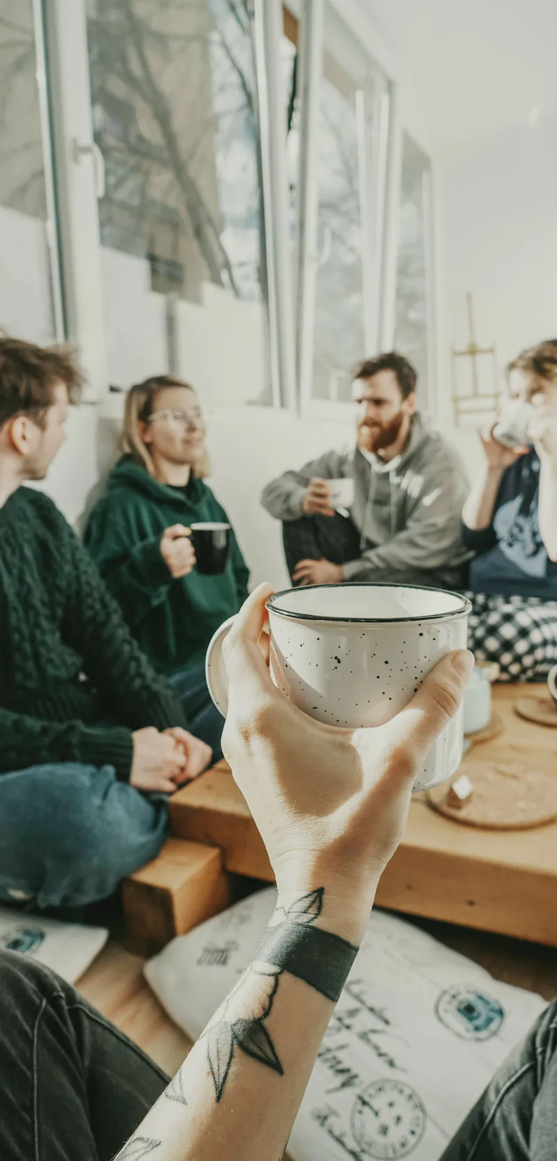 Four people sitting together with mugs of tea, mid-conversation, seen past a raised cup.
