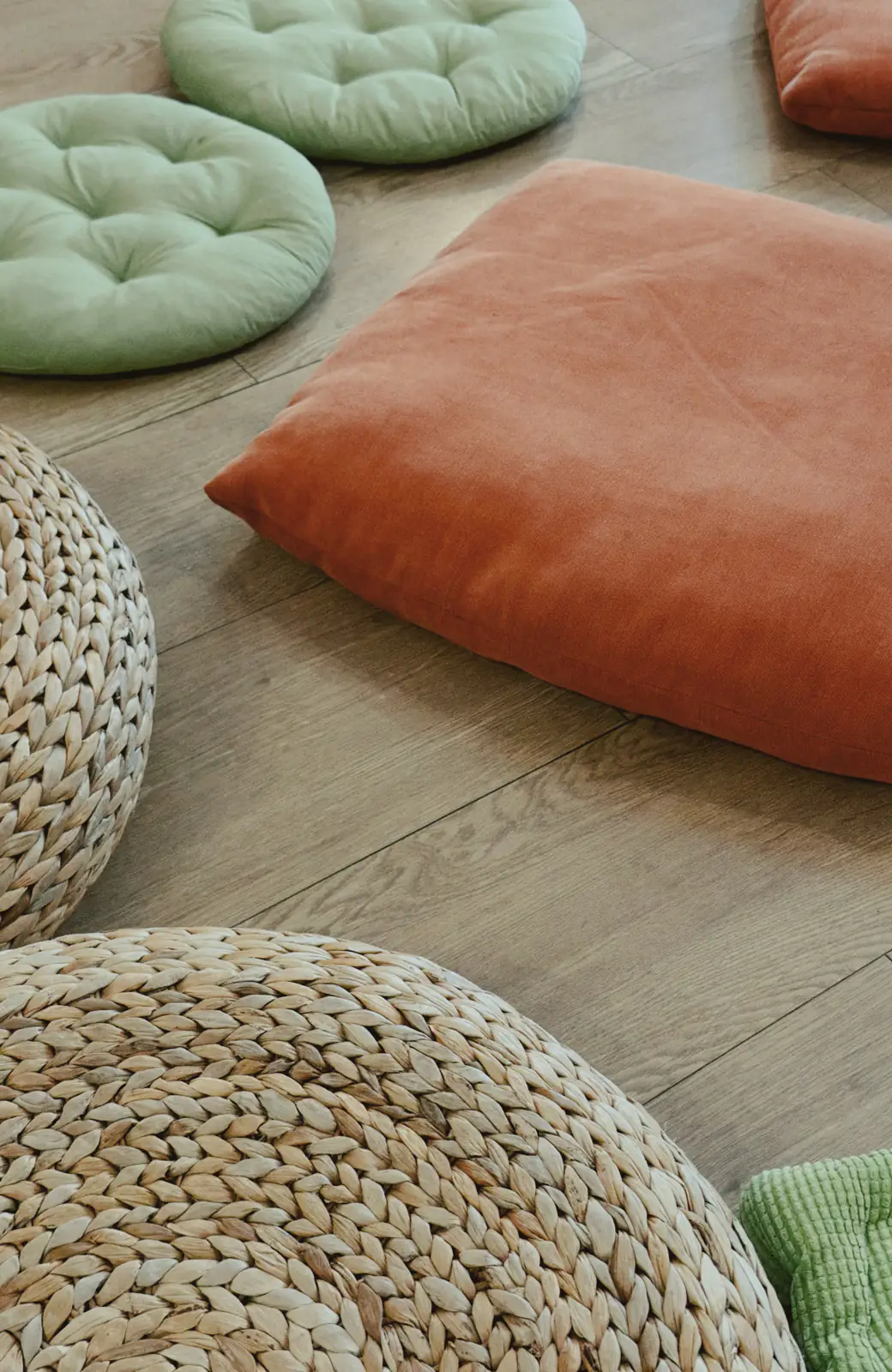 Round meditation cushions and woven floor poufs laid out on a wooden floor.