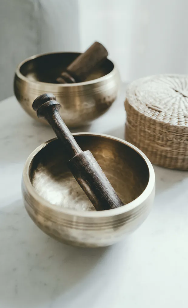 Two brass singing bowls with wooden strikers resting on a pale table.